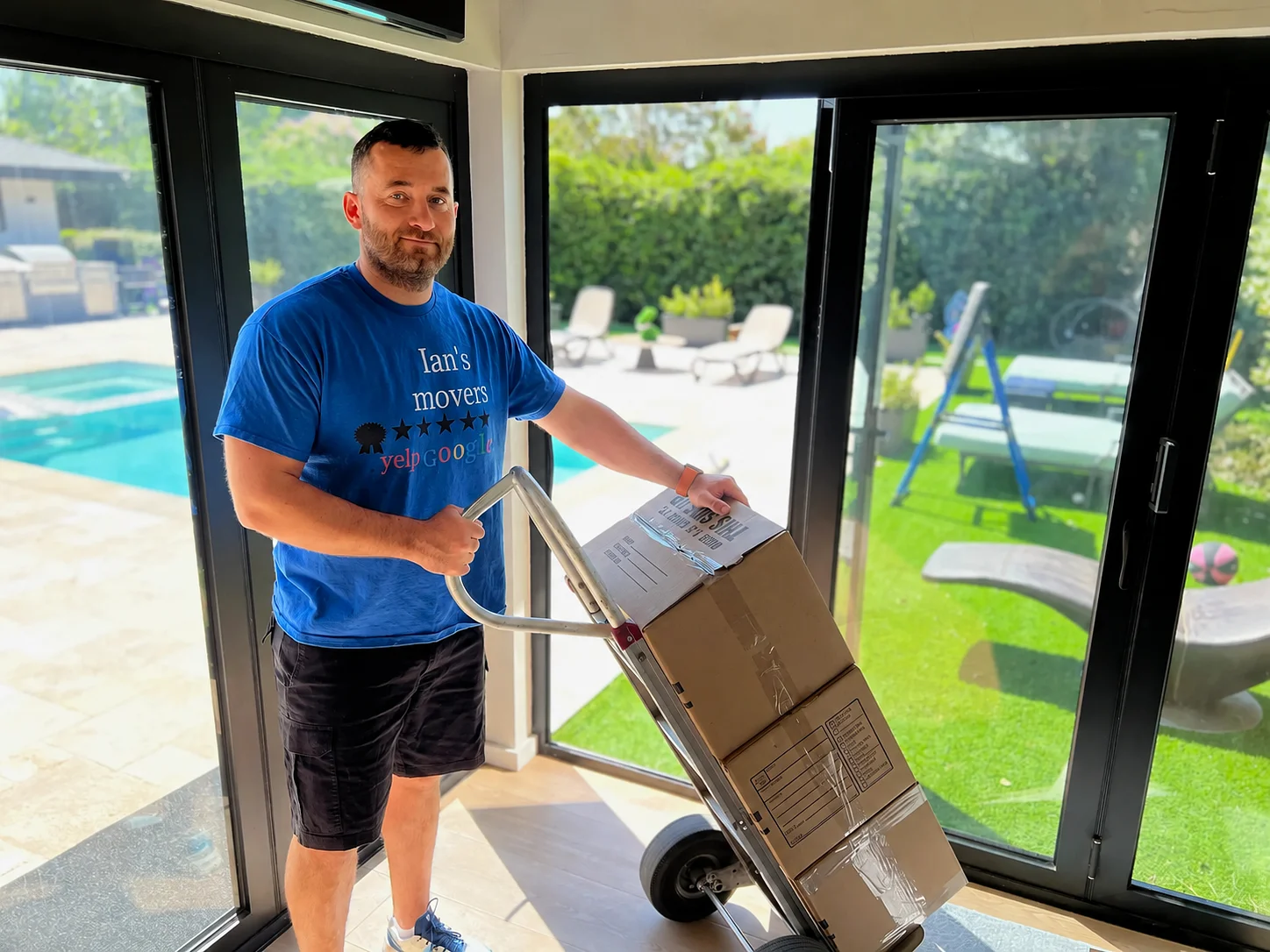 Ian's Movers mover transporting packed boxes on a dolly inside a home